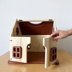 a hand is holding the door to a wooden dollhouse with windows and doors on it