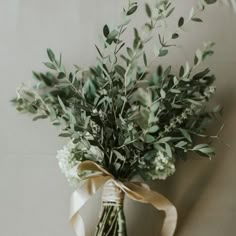 a bouquet of greenery tied to a white wall with a brown ribbon around it