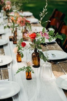 the table is set with several vases filled with flowers and greenery on it