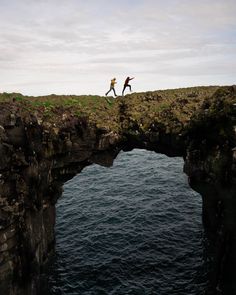 two people jumping off the edge of a cliff into the ocean from a bridge over water