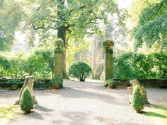 two statues in the middle of a garden with trees and bushes behind them, all facing different directions