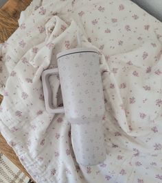 a white coffee cup sitting on top of a bed next to a blanket and pillow