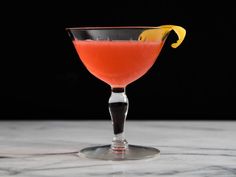 an orange cocktail in a coupe glass with a lemon wedge on the rim and garnish