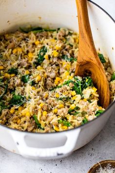 a pot filled with rice and vegetables on top of a white counter next to a wooden spoon