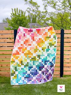 a multicolored quilt hanging on a fence in front of a wooden privacy wall