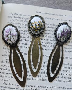 three brooches with flowers on them sitting on top of an open book,