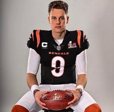 a man holding a football sitting on top of a chair in front of a gray background