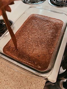 someone is cutting into a brownie in a glass dish on the stove top with a knife