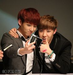 two young men posing for the camera with their cell phones in front of each other