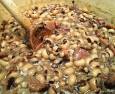 beans and meat are being cooked in a pot with a wooden spoon on the side