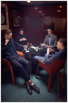 three men sitting at a table playing cards in a room with dark walls and green carpeting