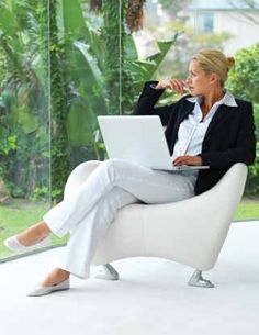 a woman sitting in a white chair with a laptop on her lap and looking out the window