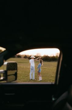 two people are playing frisbee on the grass in front of a car window