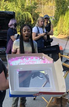 a group of people standing around a cardboard box that has been decorated with pink and white paint