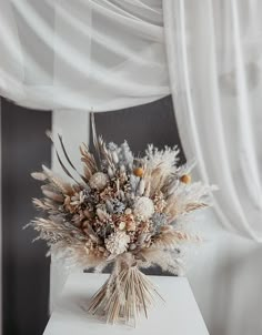 a bouquet of dried flowers sitting on top of a white table next to a curtain