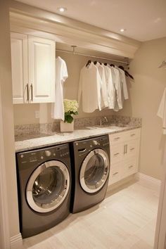 a washer and dryer in a room with white cabinets, drawers and clothes hanging on the wall