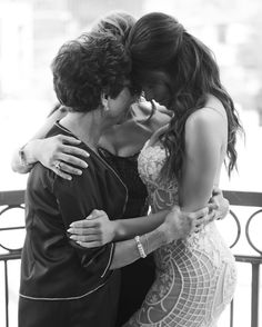 two women are hugging each other in front of a fence and railing, one woman is wearing an evening gown