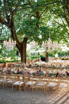 an outdoor dining table with chandeliers and flowers in the center is surrounded by trees