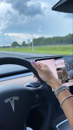 a woman driving a car with her hand on the steering wheel while looking at an electronic device