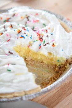 a pie with white frosting and sprinkles is on a wooden table