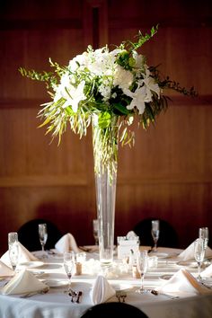 a tall vase filled with white flowers sitting on top of a table covered in plates and napkins