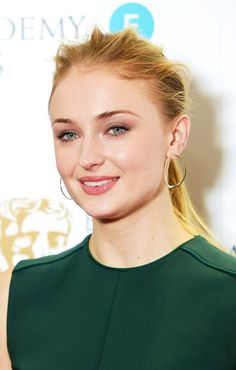 a woman with blonde hair wearing large hoop earrings and green dress smiling at the camera