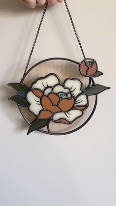 a hand holding a stained glass flower hanging from a chain on a white wall in the shape of a circle