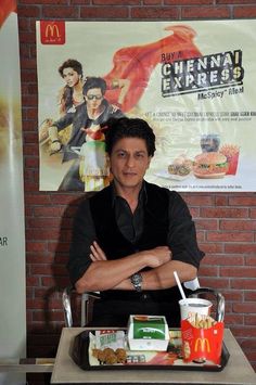 a man sitting at a table in front of a mcdonald's sign with his arms crossed