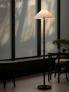 a lamp is sitting next to a table in front of a window with large windows