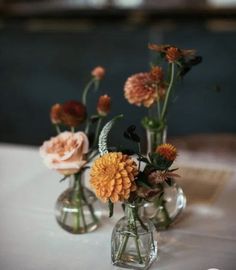 three vases filled with flowers sitting on top of a white tablecloth covered table