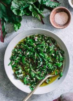 a white bowl filled with green vegetables next to some spices and seasonings on a table