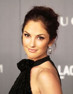 a woman in a black dress smiling at the camera with her hair pulled back into a bun