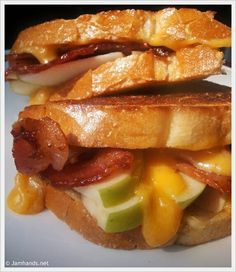 two sandwiches with bacon, cheese and apple slices on them sitting on a white plate