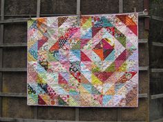 a person holding up a colorful quilt on top of a wooden deck in front of some trees