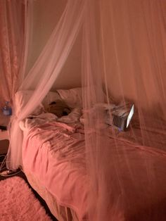 an unmade bed with pink bedspread and mosquito netting on the headboard