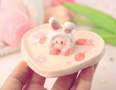 a hand holding a small ceramic pig in a heart shaped box with flowers on it