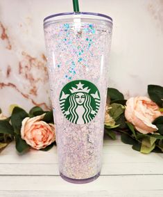 the starbucks cup has glitter on it and is next to some pink roses with green straws