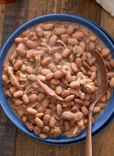 a blue bowl filled with beans on top of a wooden table next to a spoon