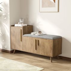 a wooden bench sitting in front of a white wall next to a rug and potted plant