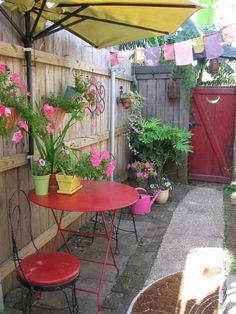 an outdoor table and chairs with flowers in pots on the side walk way next to a wooden fence