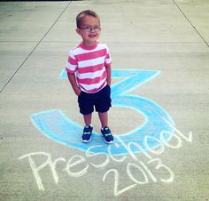 a little boy standing in front of a chalk drawing on the sidewalk with his name written