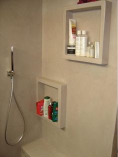 a white toilet sitting next to a shower in a bathroom under a shelf filled with personal care items