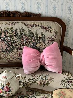 a pink bow tie sitting on top of a couch next to a tea pot and spoon