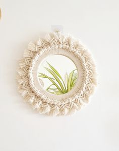 a round mirror hanging on the wall with a plant in it's center,