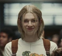 a woman with blonde hair wearing a white t - shirt and brown suspenders smiles at the camera