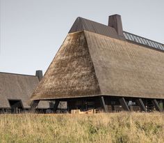 an old building with thatched roof sitting on top of a grass covered field