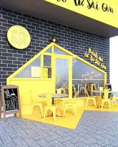 a yellow building with tables and chairs in front of it on the side of a brick wall