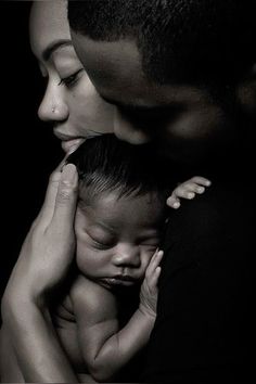 a black and white photo of a woman holding a baby in her arms while the man holds his head