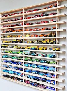 a wooden shelf filled with toy cars on top of a white wall next to a window