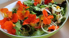 a green bowl filled with salad and orange flowers